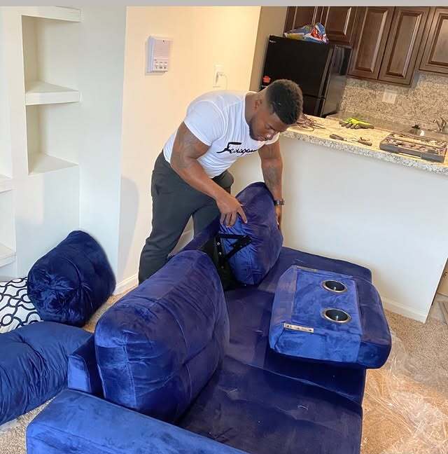 Mover building a blue sectional couch in a customer's living room