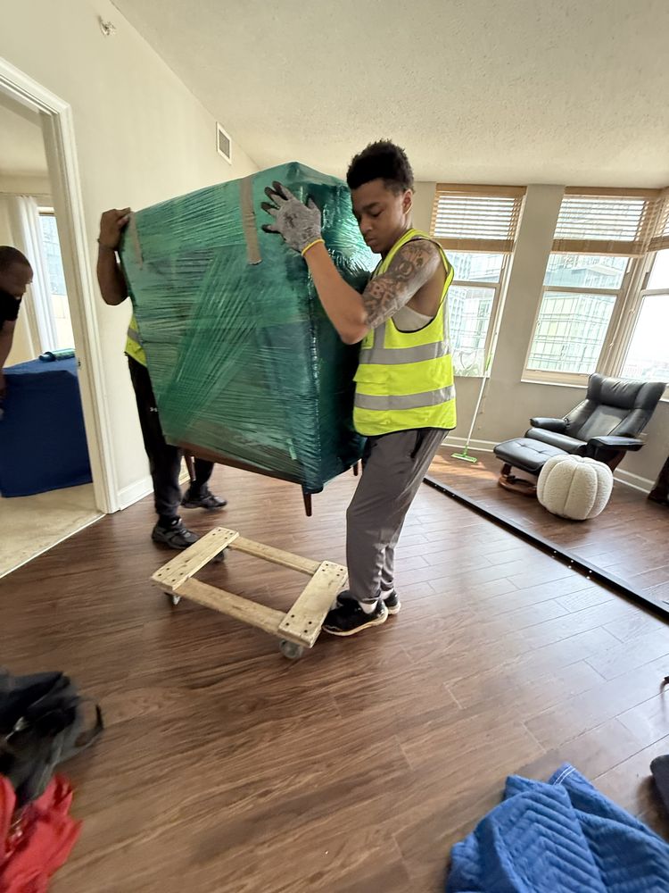 Two movers carrying a wrapped cabinet onto a dolly