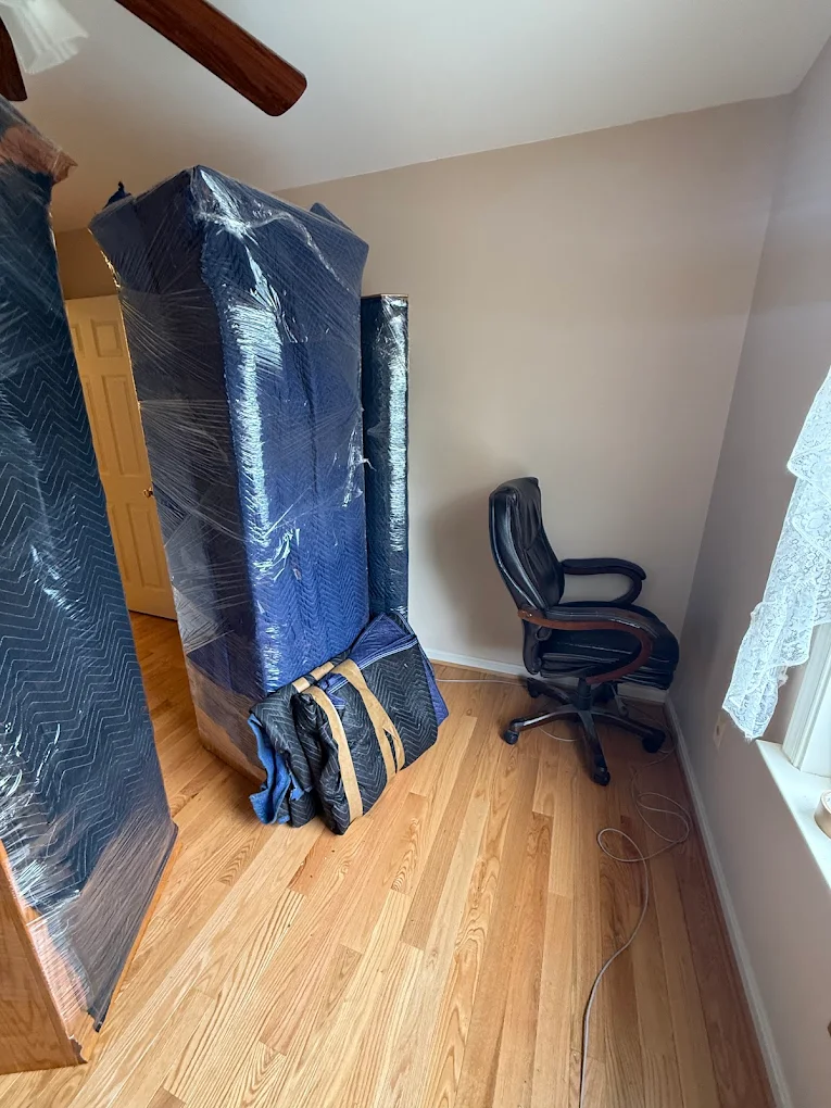 Mattress and furniture standing wrapped in navy blankets and plastic in an empty bedroom