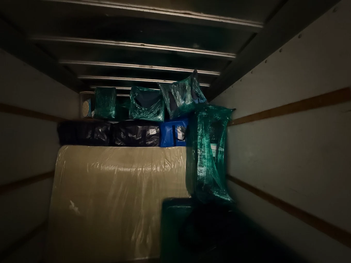Interior of the truck at night, packed with wrapped furniture lit by a work light