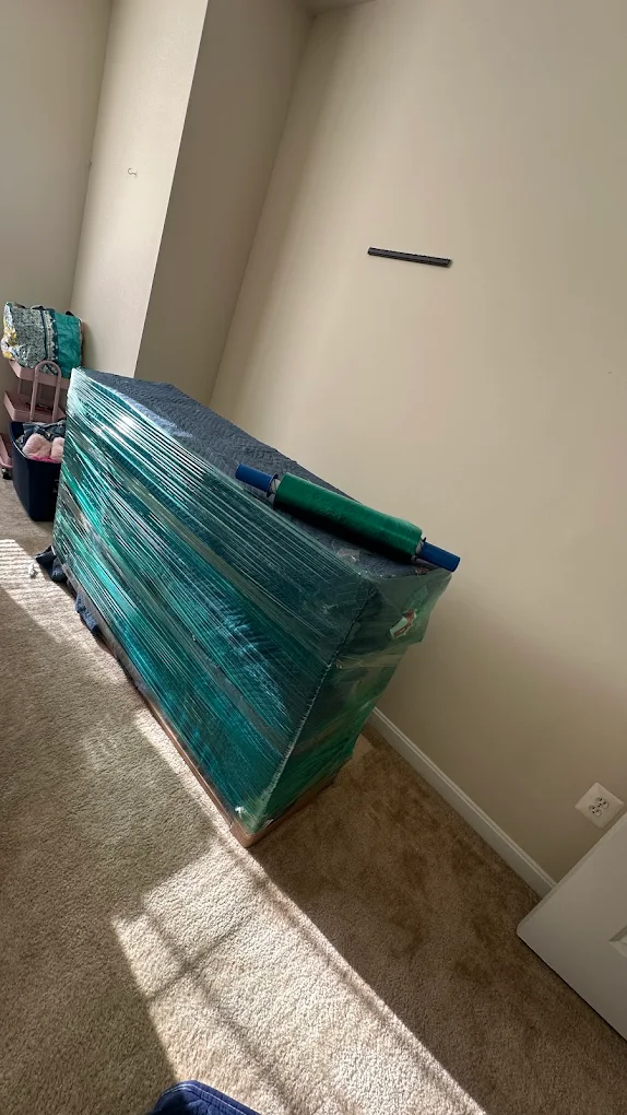 A dresser laid on a dolly wrapped in blankets and green stretch wrap with a spare wrap roll on top