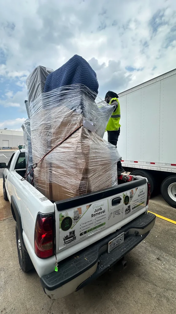 Pickup truck loaded high with wrapped furniture for junk removal, crew member strapping it down