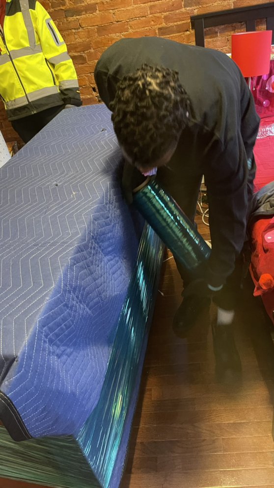Mover shrink-wrapping a blanket-covered mattress on site