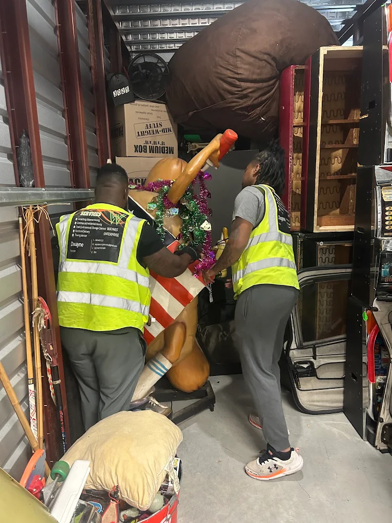 Two crew members in Wayne's Enterprise vests lifting a life-size carousel horse in a storage unit