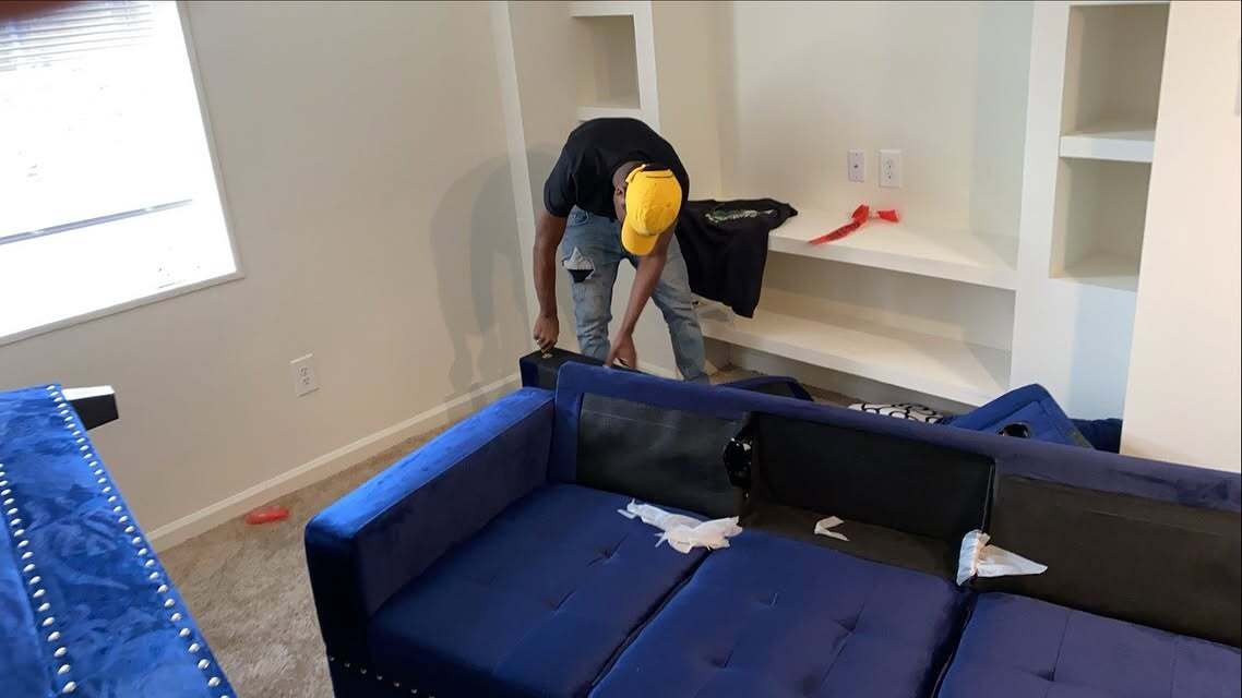 Crew member setting up a blue velvet sectional in a bright new apartment