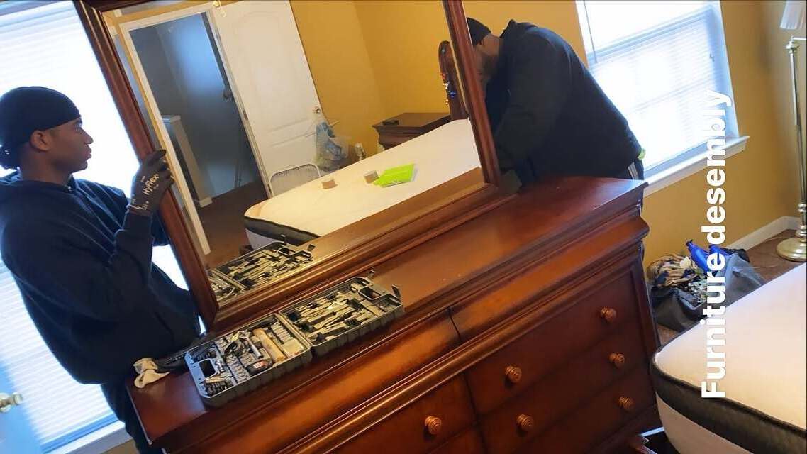 Two movers disassembling a solid wood dresser