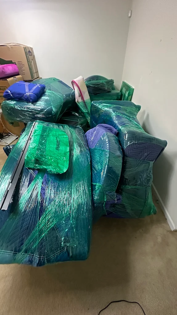 A room full of furniture sealed in green stretch wrap over blue moving blankets