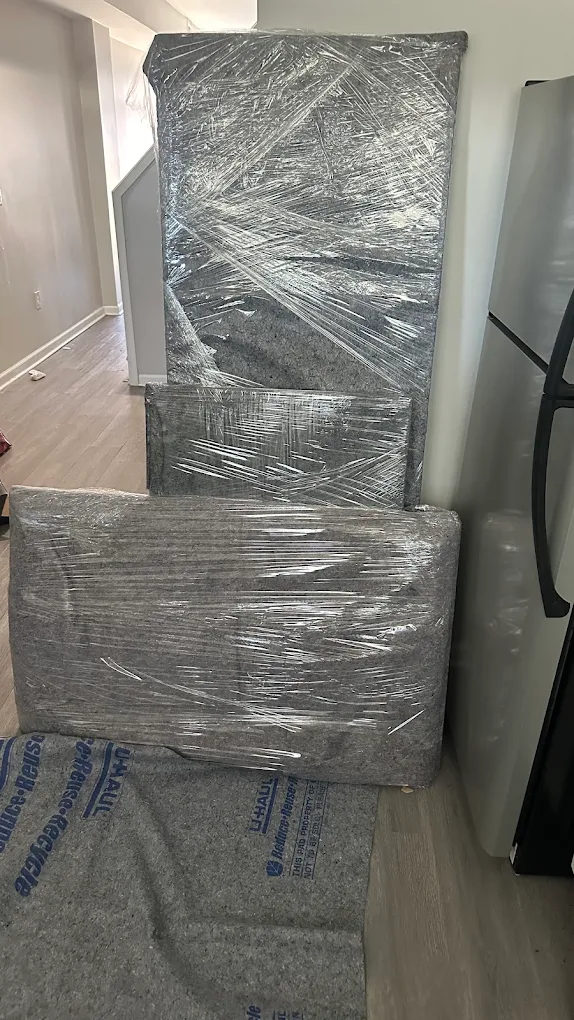Blanket-wrapped mattress, box spring and headboard staged in a hallway on floor runners