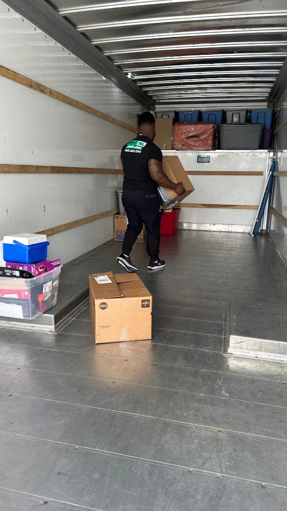 Crew member carrying a box into an empty, swept truck with totes staged along the wall